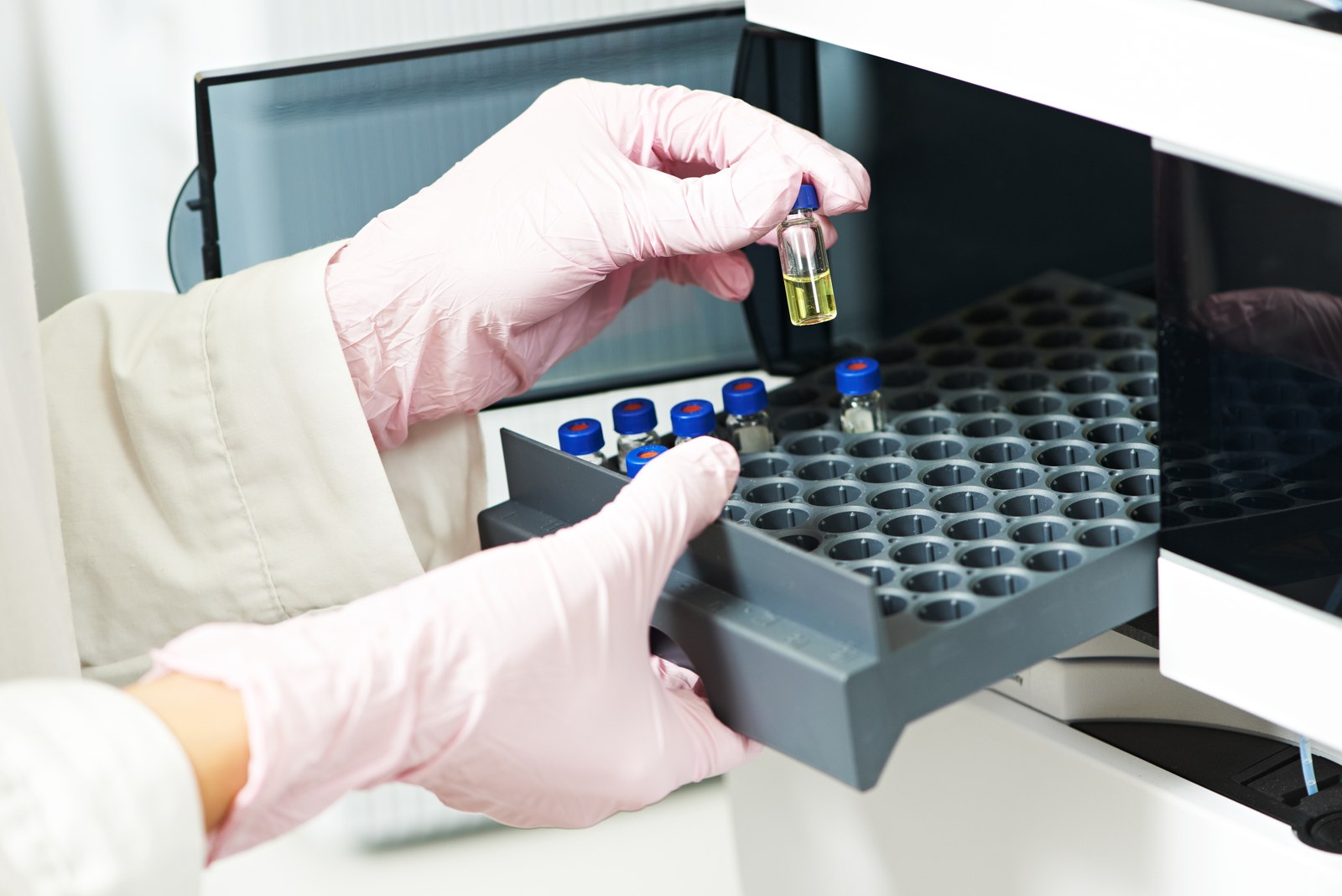 Gloved hands placing a sample vial in an analytical instrument